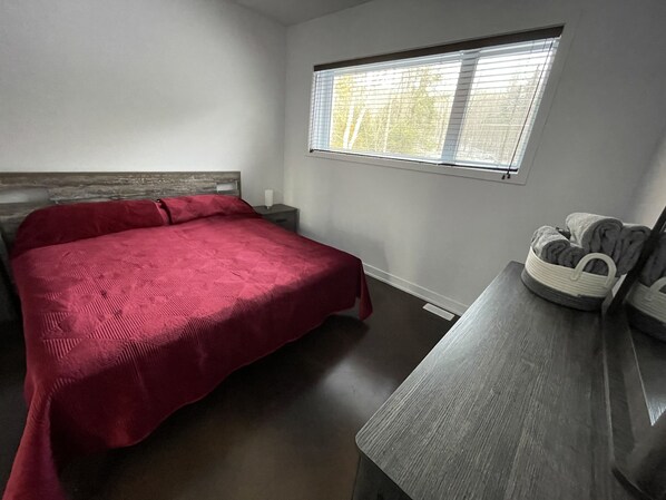 A bedroom with a bed, a nightstand, a window, and a wooden bench. - Cottage / Lake House - New - Beautiful views - Clean and comfortable (Val-des-Monts)