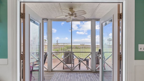 A view from inside a room to an outdoor deck with a ceiling fan, a wooden deck, and a view of the beach. - Bayfront Cottage with Screened Porch (Port St Joe)