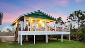 A two-story building with a green roof and white exterior, featuring a balcony with railings and a covered area with chairs and tables. - Bayfront Cottage with Screened Porch (Port St Joe)