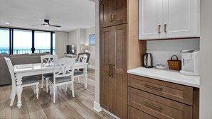 Eine moderne Küche mit weißen Schränken, ein Essbereich mit weißem Tisch und Stühlen und Meerblick durch große Fenster.