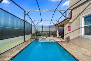 A swimming pool with a glass enclosure, a hot tub, and a patio area with outdoor furniture.