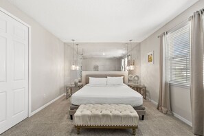 A bedroom with a large bed, bedside tables, a bench, and a window with curtains.