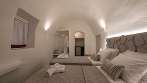 A modern hotel room with two beds, a small window with a curtain, a wall-mounted light, and a unique textured headboard. - OUTOPOIA (Santorini)