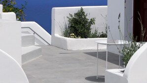 A white building with a concrete floor and a view of the sea. - OUTOPOIA (Santorini)