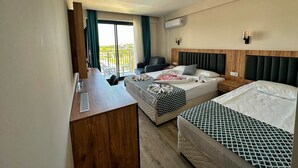 Quarto de hotel com duas camas, uma escrivaninha, uma cadeira e uma varanda com vista.