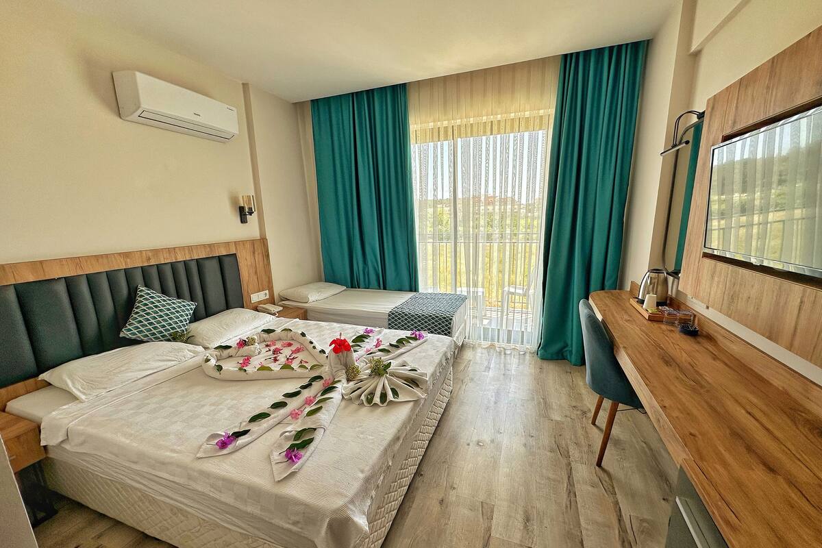 Une chambre d’hôtel avec deux lits, un bureau en bois, une télévision et un balcon avec des rideaux.