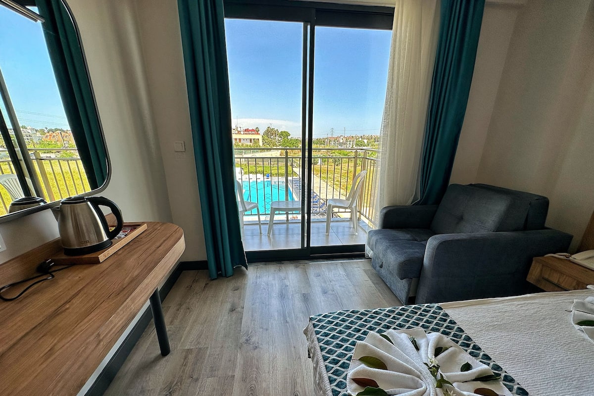 Une chambre d’hôtel avec un banc en bois, une table avec une serviette, un canapé et une vue sur une piscine, visible à travers une porte coulissante.