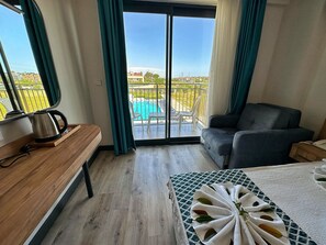 Habitación de hotel con un banco de madera, una mesa con una toalla, un sofá y vistas a una piscina a través de una puerta corredera.