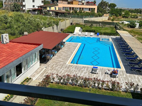 Una piscina con solárium de baldosas, sillas de descanso y un restaurante con terraza.