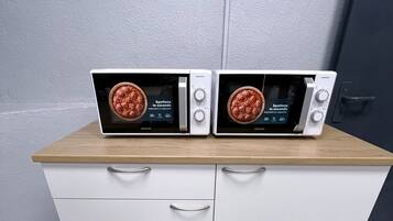 Two wall-mounted microwaves on a wooden countertop above a white cabinet with drawers.