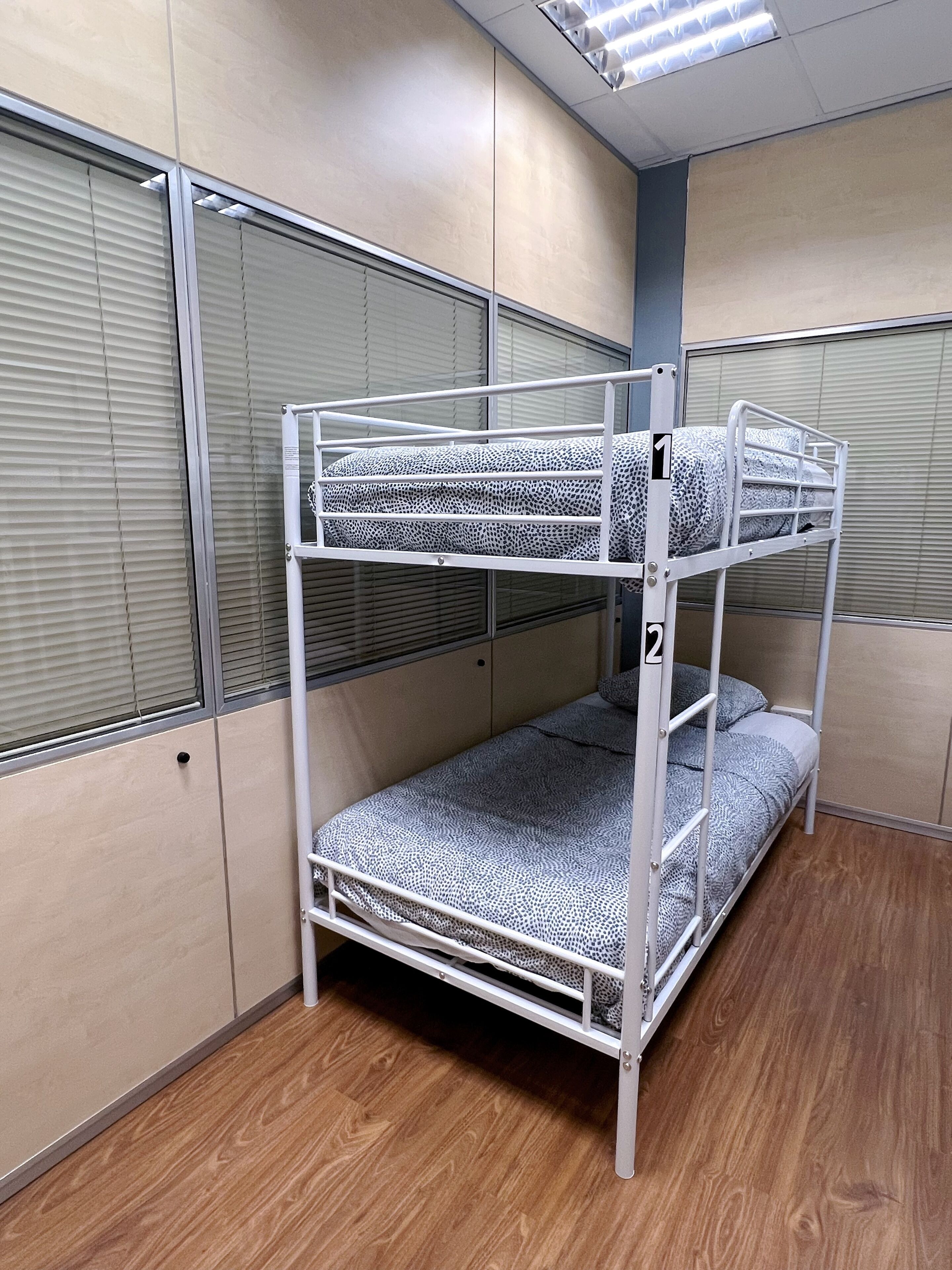 A bunk bed with a patterned mattress, a wooden floor, and a window with blinds.