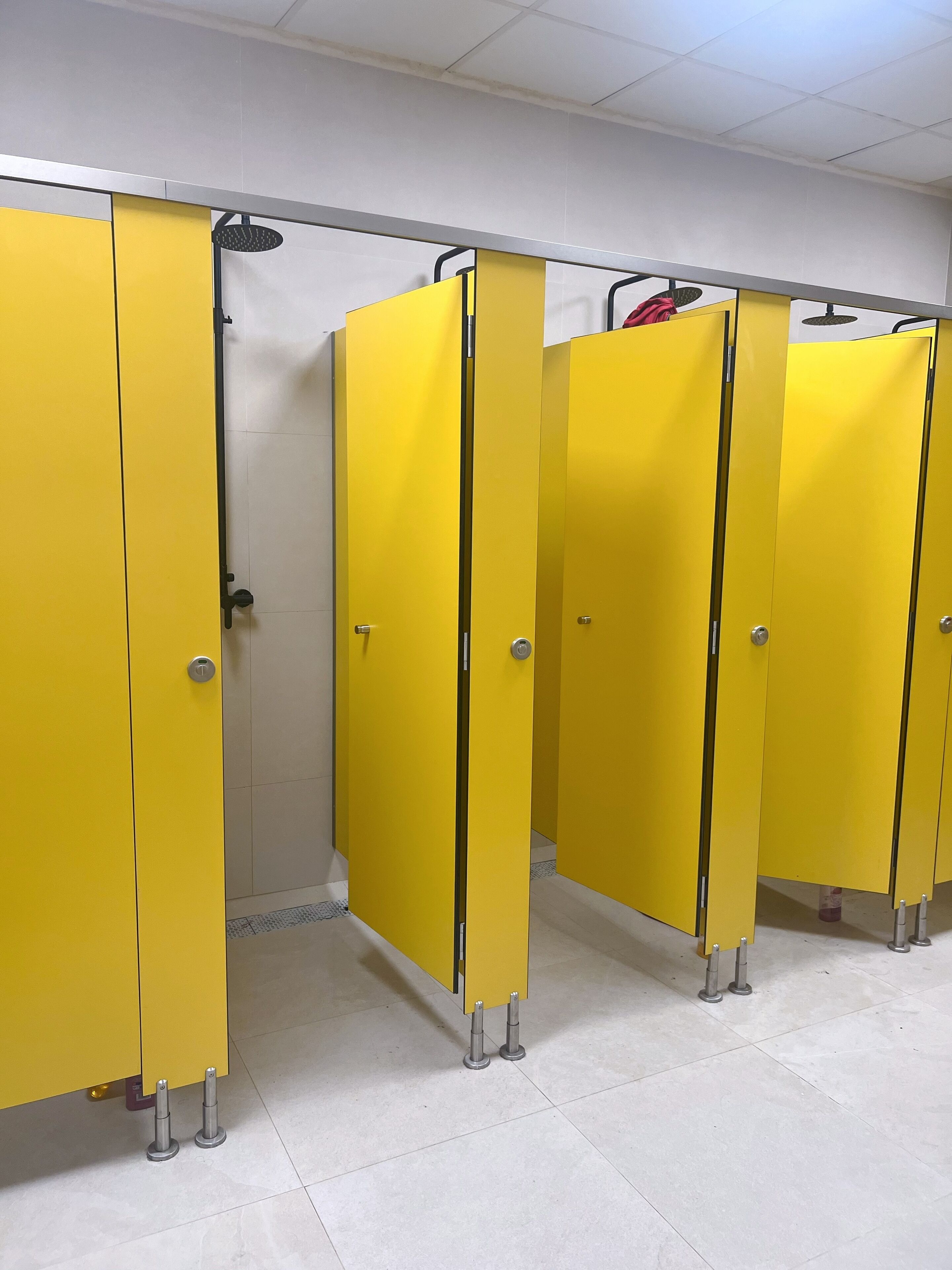 Eine Reihe von gelben, durch Wände getrennten Toilettenkabinen mit Metallgriffen und einem Fliesenboden.