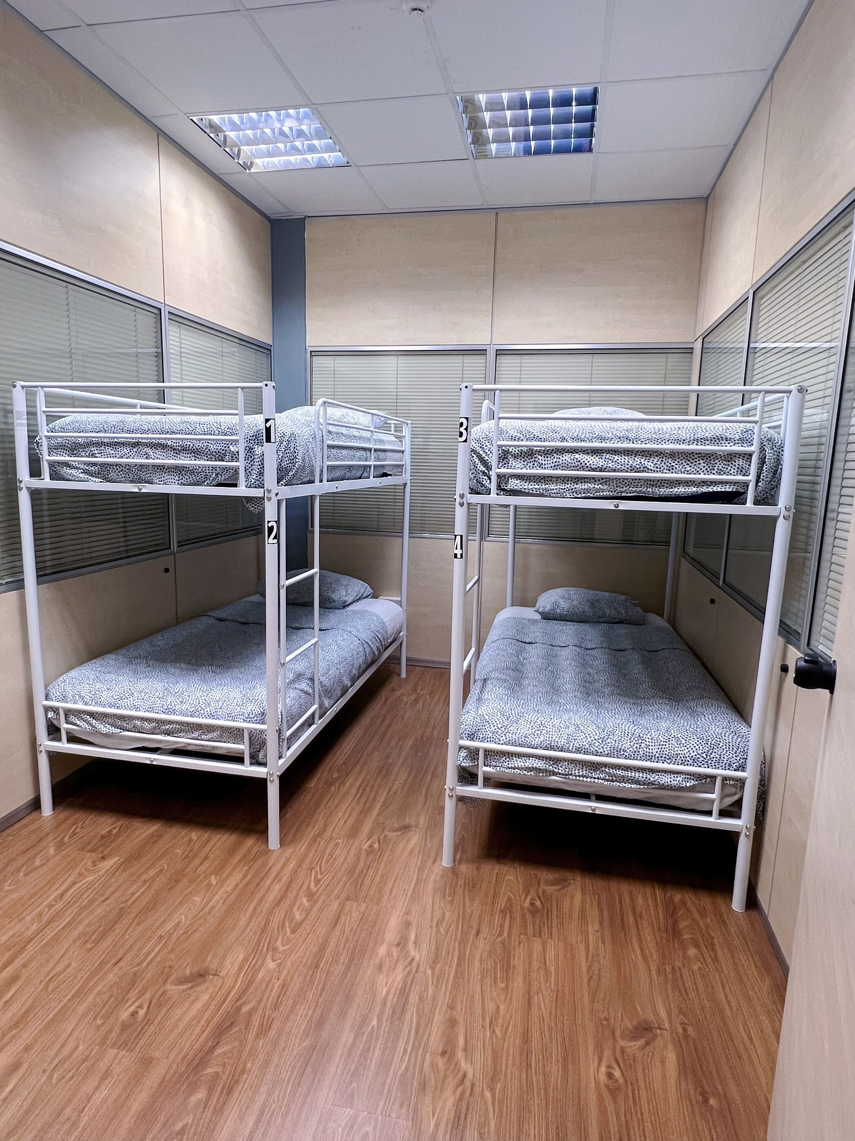 Quarto com beliches, piso de madeira e janela com persianas.