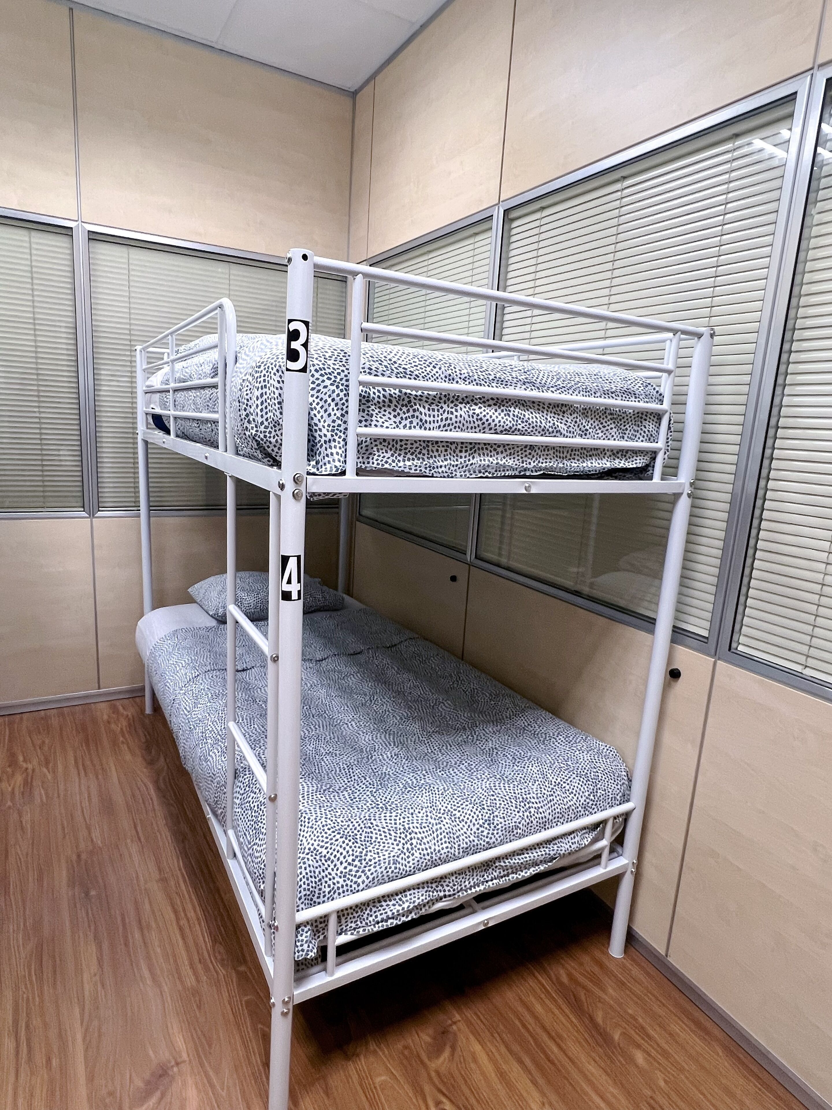 A bunk bed with two levels, numbered 3 and 4, in a room with beige walls and a window with blinds.