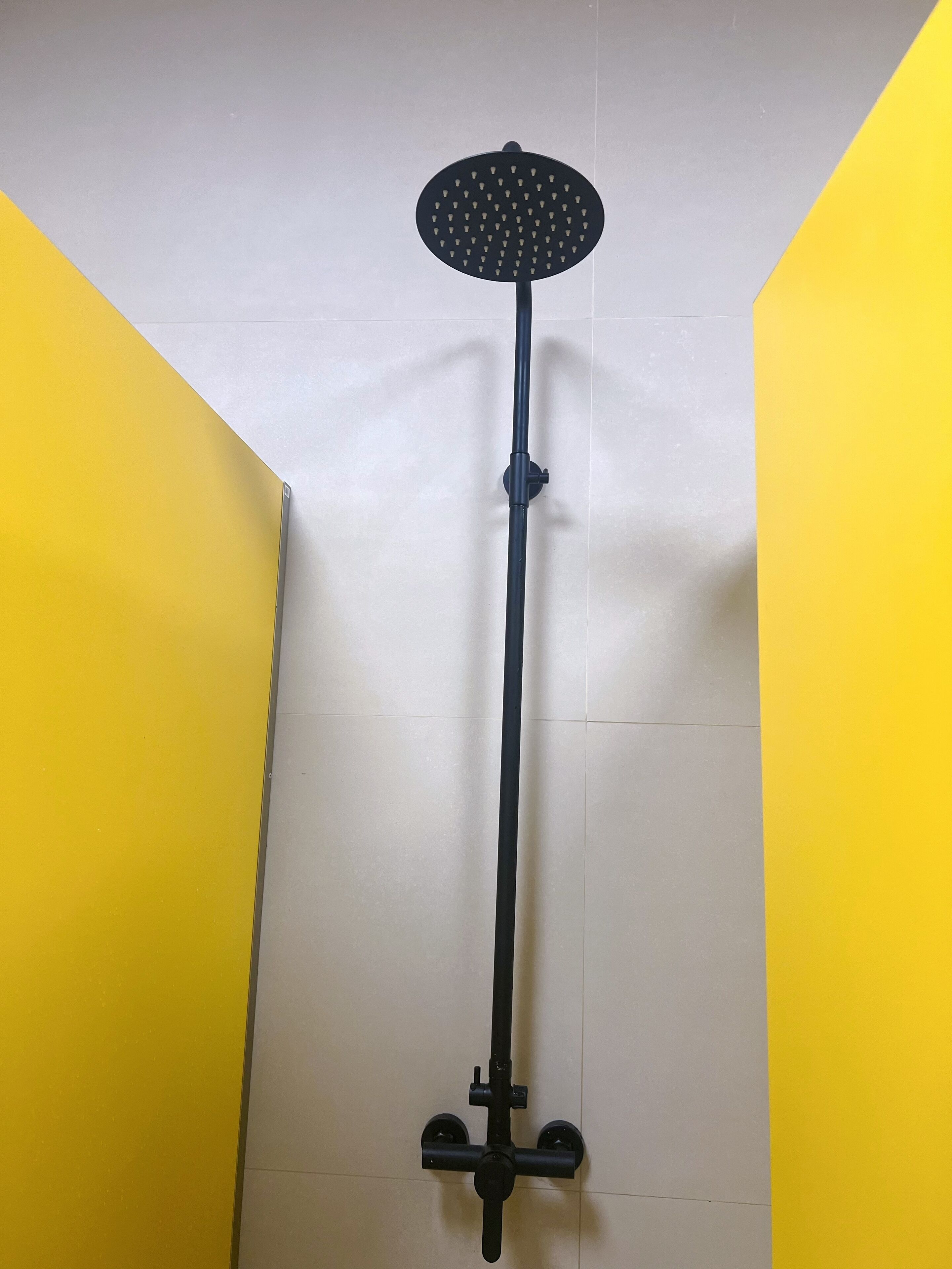 A black showerhead mounted on a wall in a bathroom with yellow and white tiles.