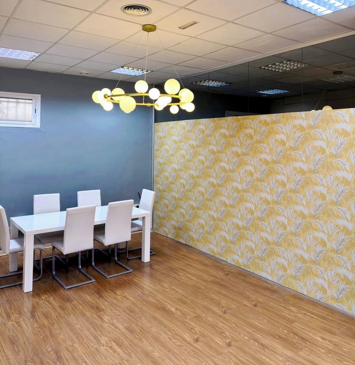 Un salón de conferencias con una mesa y sillas blancas, un divisor de ambiente con diseño y un techo con iluminación empotrada.