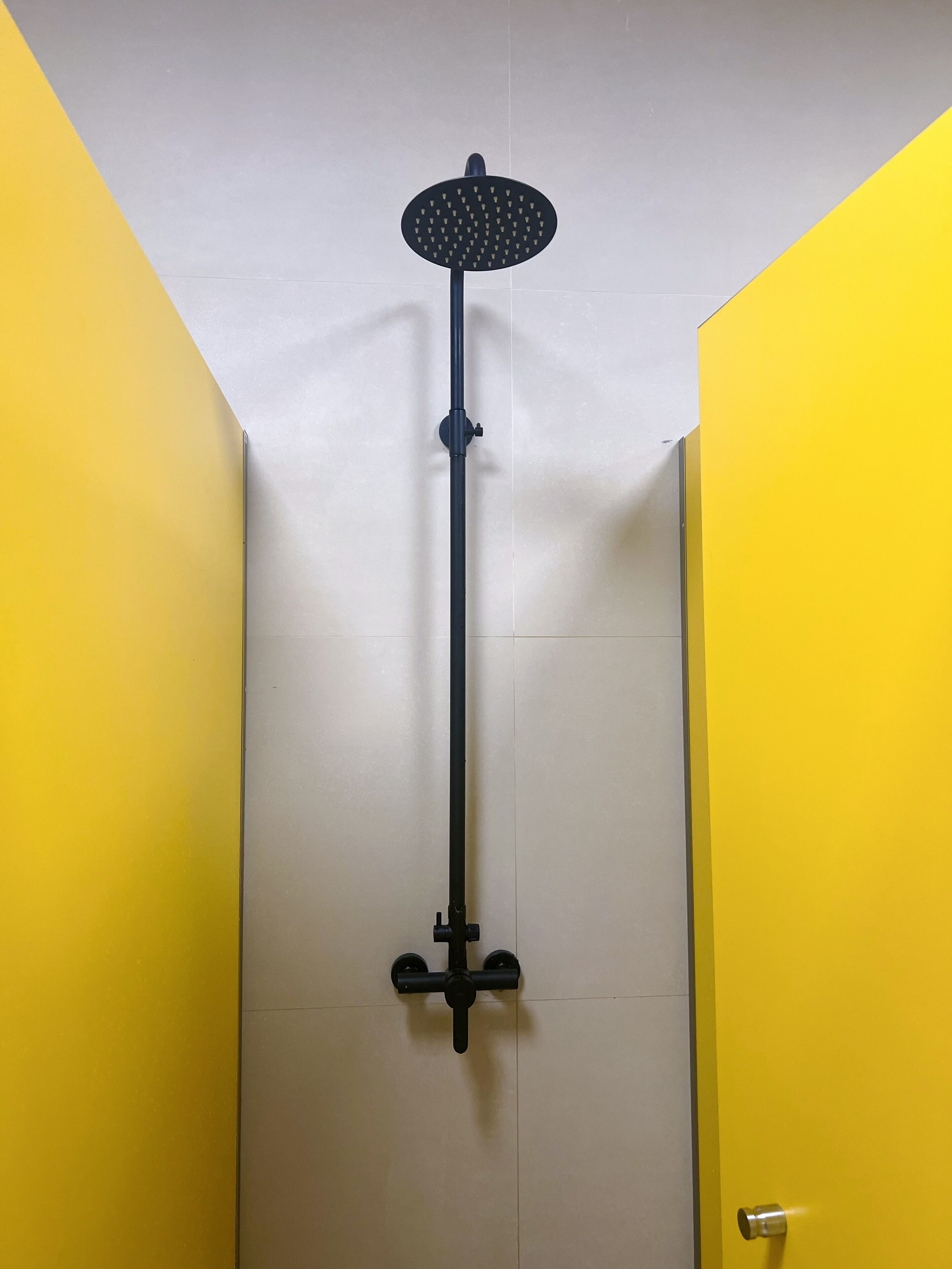 Ducha con un cabezal negro y un soporte largo de color negro en una habitación con paredes amarillas y techo blanco.
