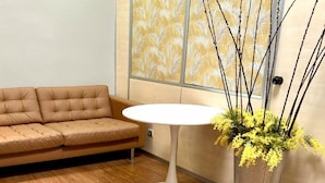 A room with a brown leather sofa, a white round table, and a potted plant with yellow flowers. - Hostel Acacias (Madrid)
