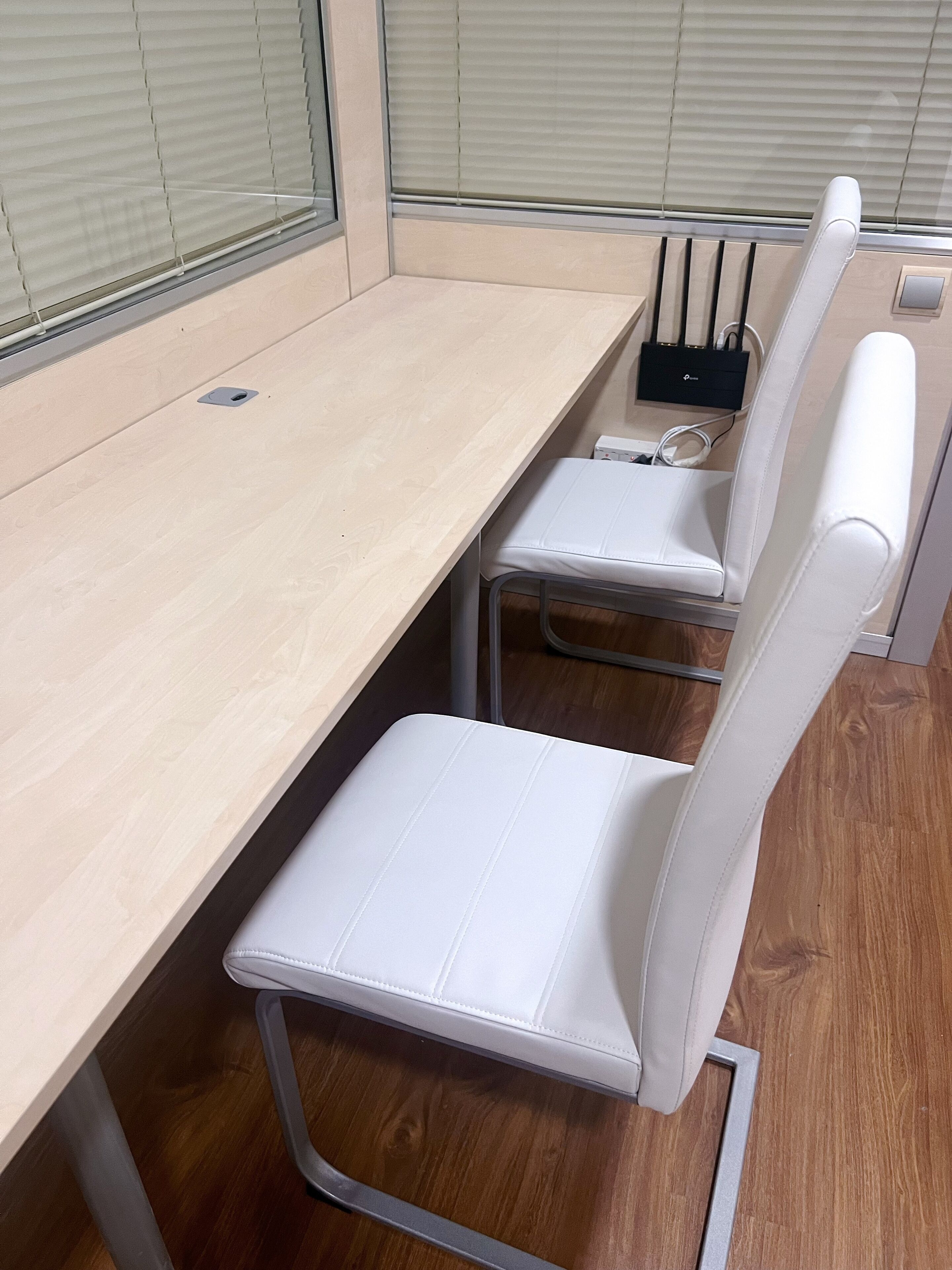 A modern office space with a wooden desk, two white chairs, and a black electronic device on the desk.