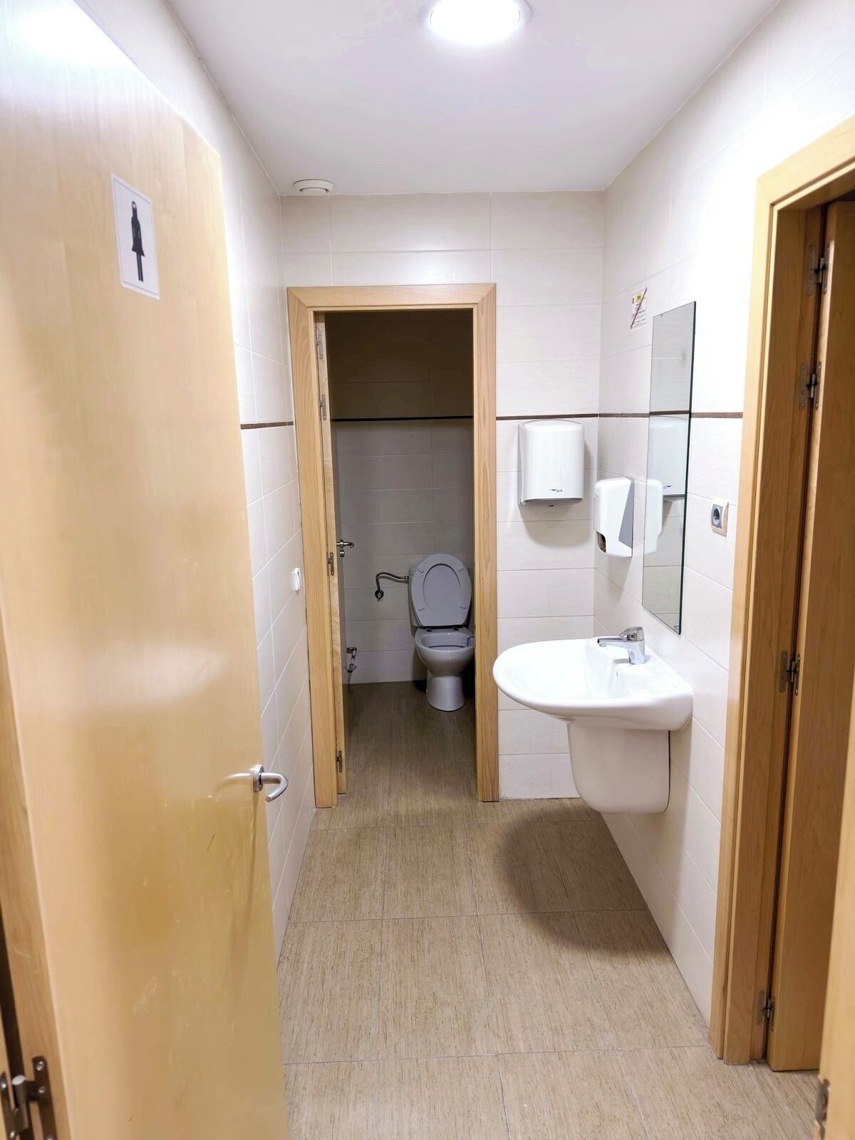 A small, clean bathroom with a toilet, sink, and mirror.