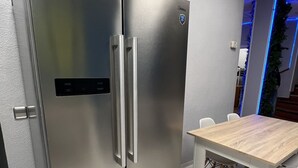 A stainless steel refrigerator with a digital display, a wooden table with chairs, and a marble floor. - Hostel Acacias (Madrid)