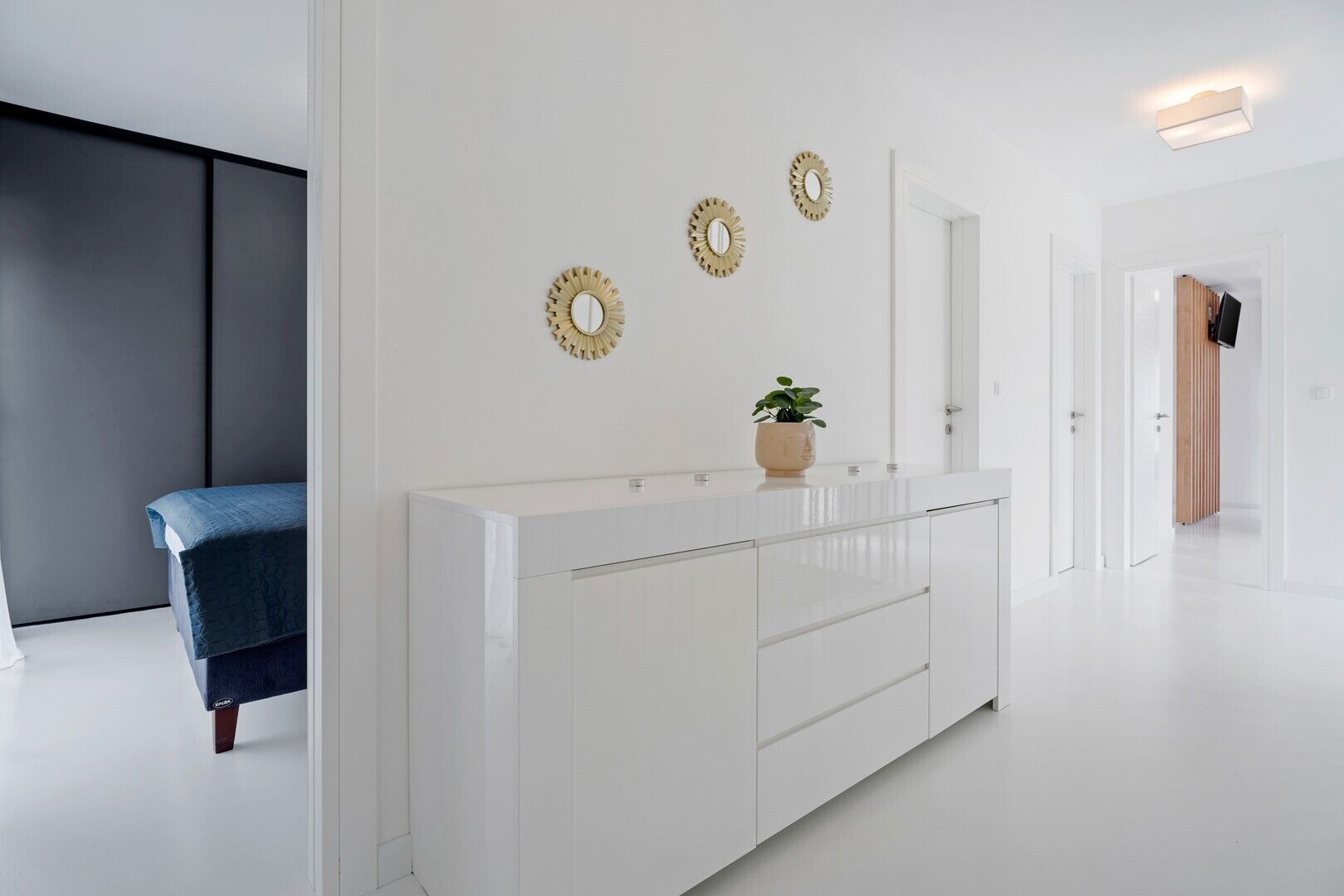 Una camera d'albergo moderna con un comò bianco, una panca blu e specchi decorativi a parete.