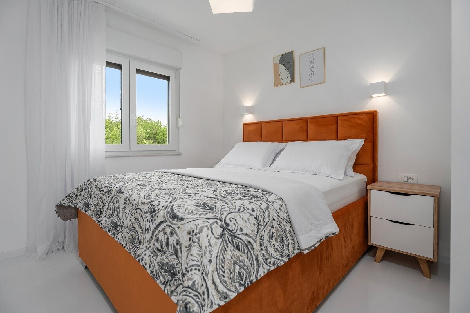 A bedroom with a bed, a nightstand, a window, and two wall-mounted lights.