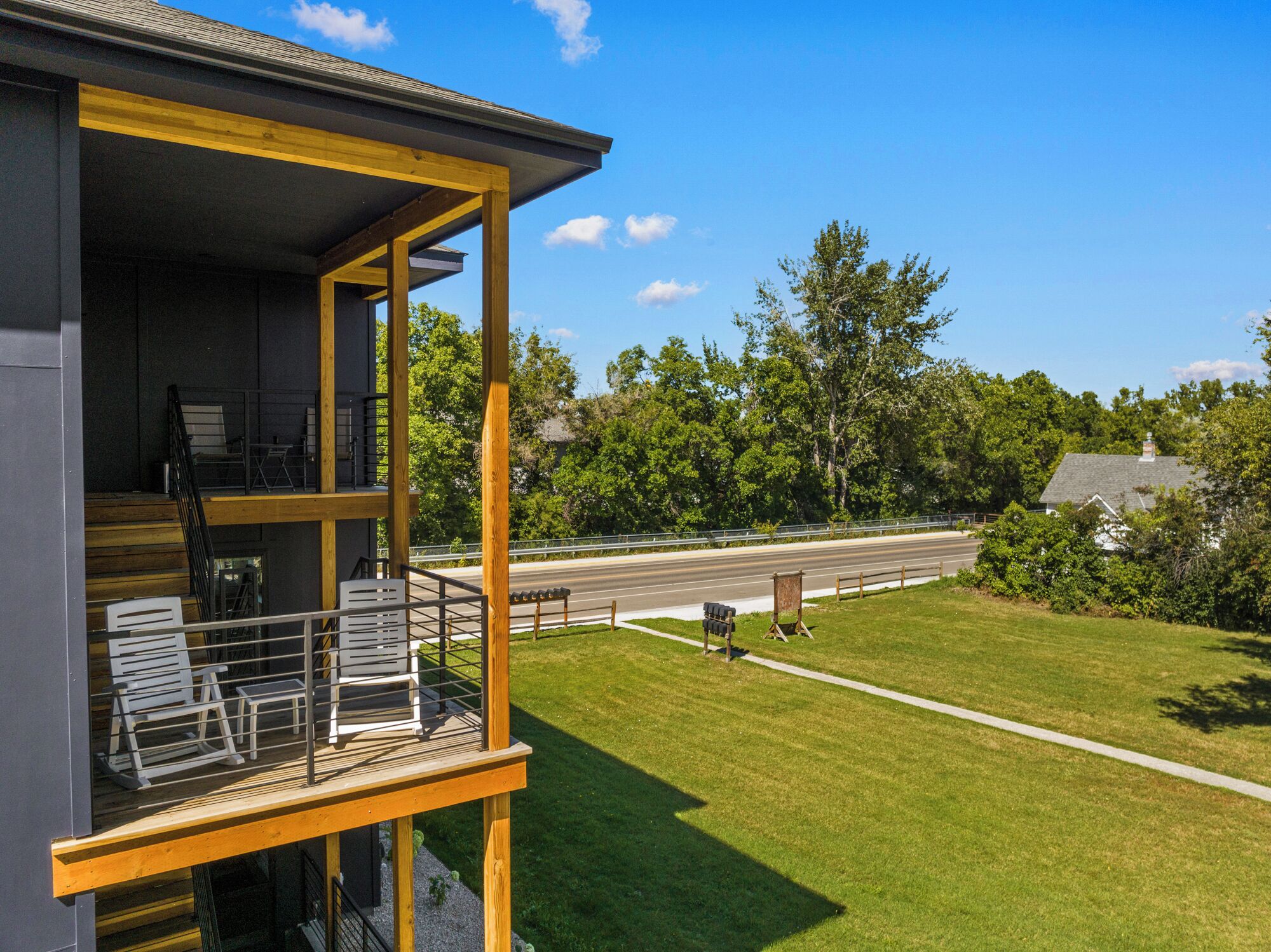 A two-story building with a balcony overlooking a road and greenery.