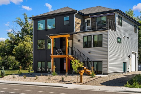 A modern multi-story house with a prominent balcony and a staircase leading to the upper floor. - Winter House - Great home located within walking distance to Main Street! (Bozeman)