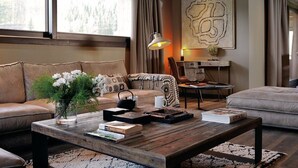 A cozy living room with a leather sofa, a wooden coffee table with books and a vase of flowers, and a large abstract painting on the wall. - Chalet Le Prariand (Megève)