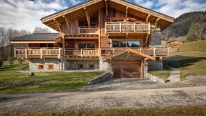 A large wooden chalet with multiple balconies, stone foundation, and a stone entrance. - Chalet Le Prariand (Megève)