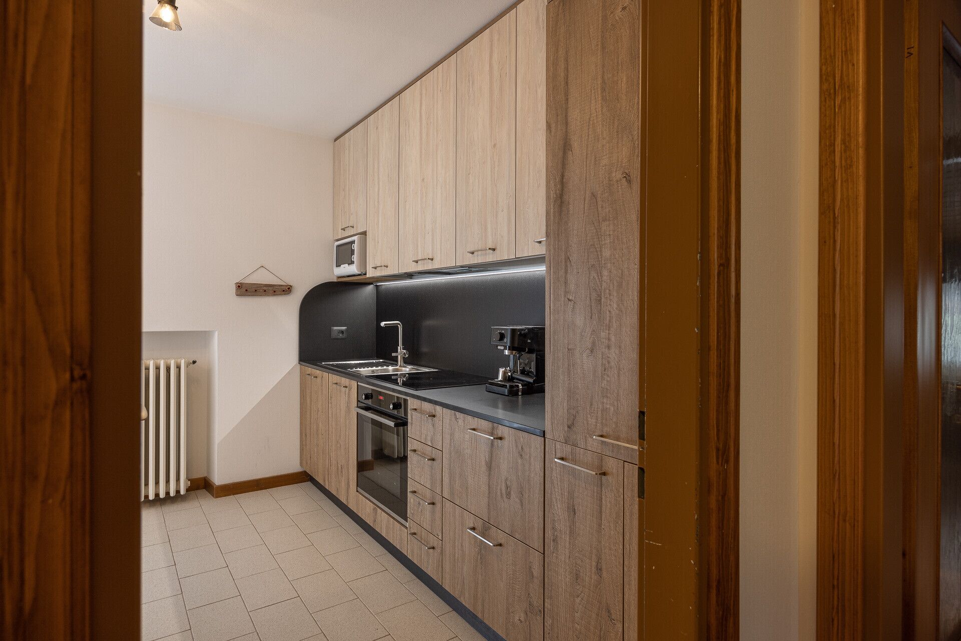A compact kitchen with wooden cabinets, a black countertop, a built-in oven, and a coffee maker.