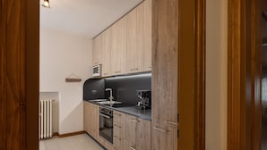 A compact kitchen with wooden cabinets, a black countertop, a built-in oven, and a coffee maker.