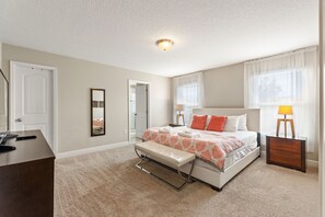 Une chambre à coucher comprenant un lit, des tables de chevet, un banc, une commode et un luminaire au plafond.
