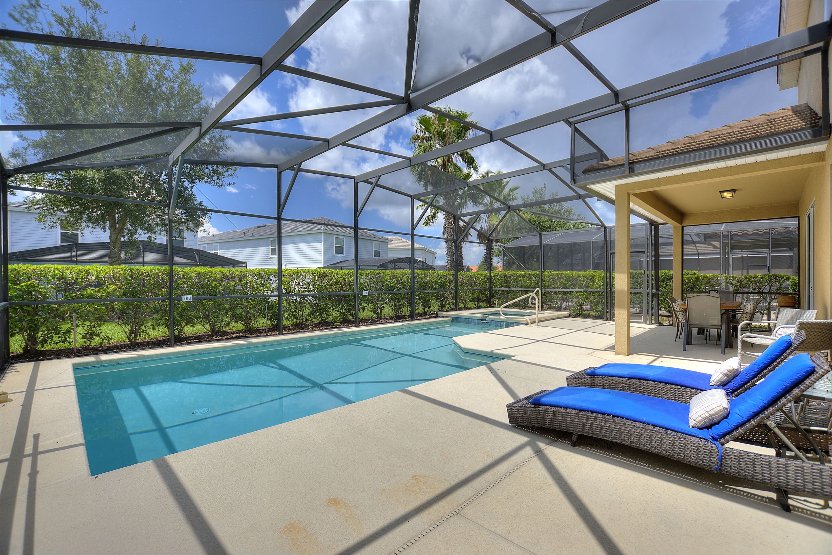 Un espace piscine doté d’une structure en verre, de chaises longues et d’une terrasse avec mobilier d’extérieur.