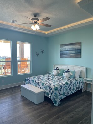 A bedroom with a bed, a ceiling fan, and a view of the outdoors through large windows.