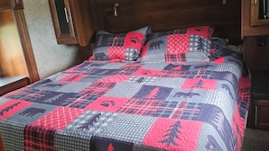 Un lit recouvert d’une couette rouge et grise ornée de motifs animaliers et d’arbres.