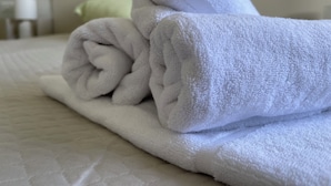 Ein ordentlich gefaltetes weißes Handtuch auf einem Bett mit einer strukturierten weißen Bettdecke.