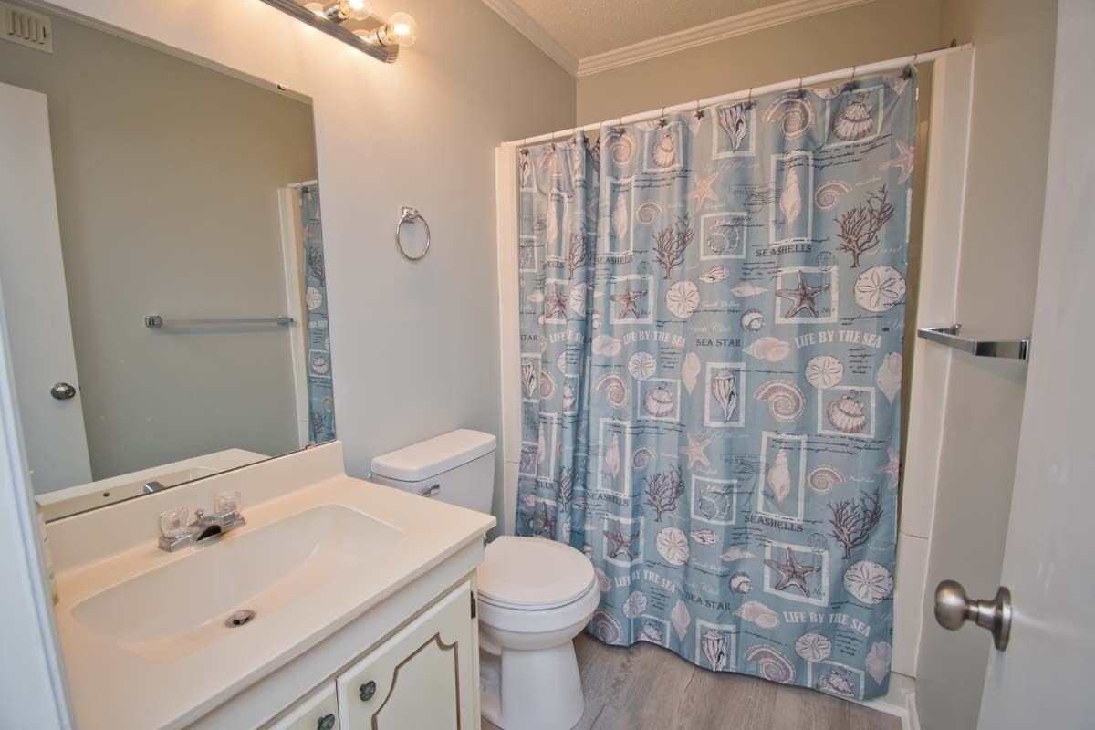 Une salle de bain avec un lavabo blanc, des toilettes et un rideau de douche orné d’un motif de coquillages.
