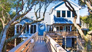 A wooden deck leading to a house with a blue exterior and a white upper level. - Seacluded Tree House, Oceanfront House in Pine Knoll Shores, NC! (Pine Knoll Shores)
