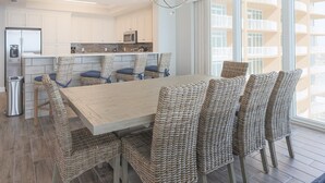 Uma cozinha moderna com armários brancos, uma ilha central e um espaço de refeições com cadeiras de vime e uma mesa de madeira.