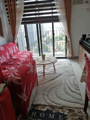 A living room with a red sofa, a small round table with a plant, and a view of buildings through large windows.