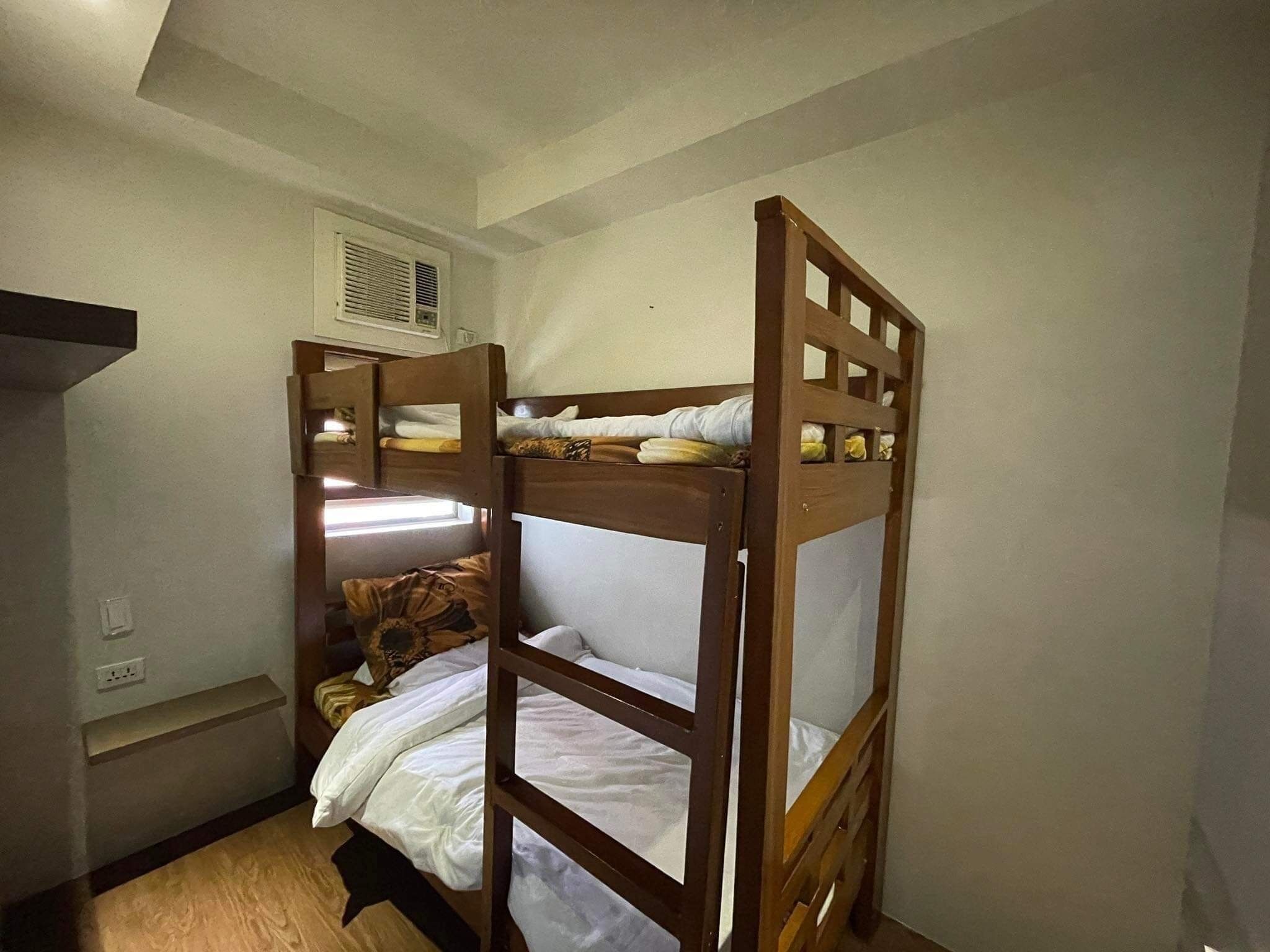 Een slaapkamer met een stapelbed, een raam, een plank en een stopcontact.