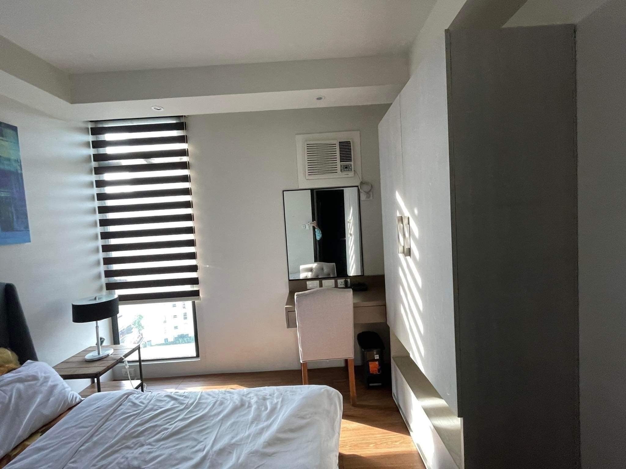 Ett hotellrum med en säng, ett skrivbord, en stol och ett fönster med persienner.