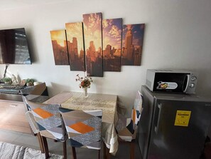 A dining area with a table set for four, a vase with flowers, and a cityscape painting on the wall.