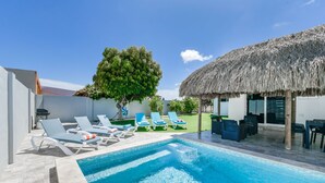 A swimming pool with lounge chairs, a thatched-roof structure, and a tree. - 3BR 2.5BA Villa w/Pool in Palm Beach (Noord)