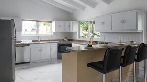 A modern kitchen with white cabinets, a central island with bar stools, a built-in oven, and a large window providing natural light. - 3BR 2.5BA Villa w/Pool in Palm Beach (Noord)