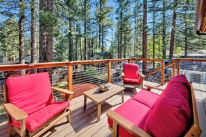 Une terrasse en bois, agrémentée de meubles rouges, dont un canapé et des fauteuils, donnant sur une zone boisée.