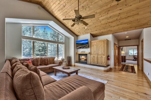 A spacious living room with a large sectional sofa, a fireplace, and a wooden ceiling.