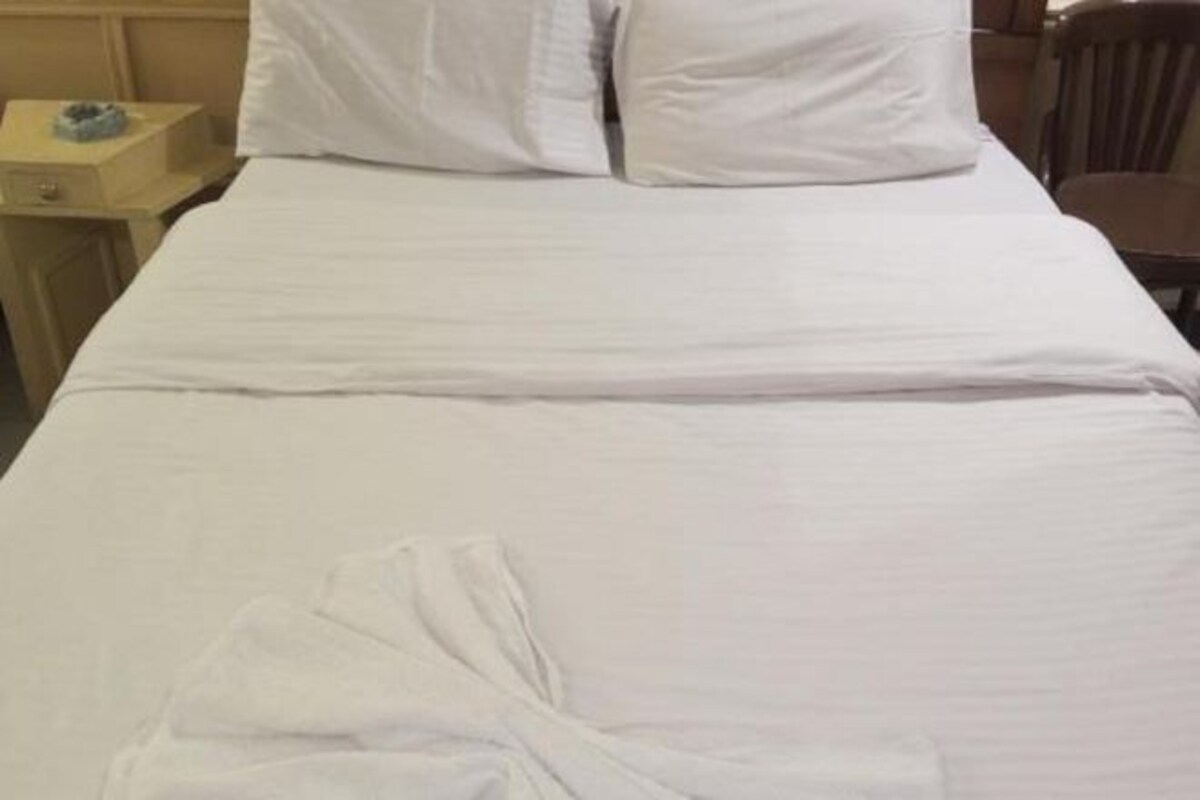 A neatly made bed with white linens, a wooden nightstand with a lamp, and a chair in a hotel room.